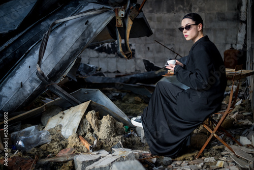 A girl dressed in black is drinking coffee in a destroyed cafe where a Russian army shell hit.