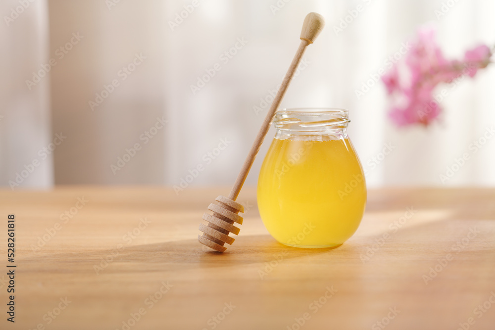 Honey background. Sweet honey in a glass jar and a honey spoon on a wooden table. Honey background. Sweet honey in a glass jar and a honey spoon on a wooden table.