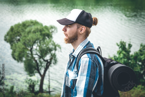 Male traveler with backpack and karimat in nature by the lake.