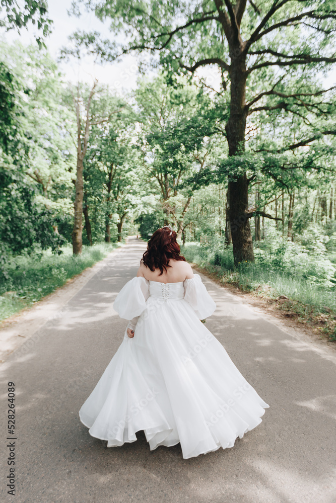 the bride is spinning in a white dress on a road in forest
