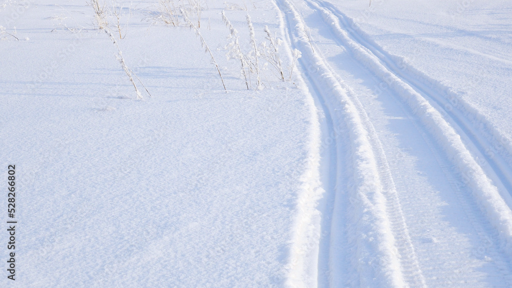 Track of traces from a snowmobile in drifts of white snow. Nature and outdoor. Winter theme wallpaper or background