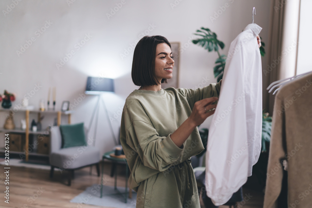 Smiling woman choosing clothes in apartment