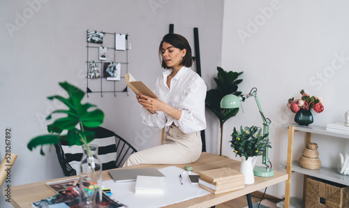 Young lady reading book aloud while working in modern workspace