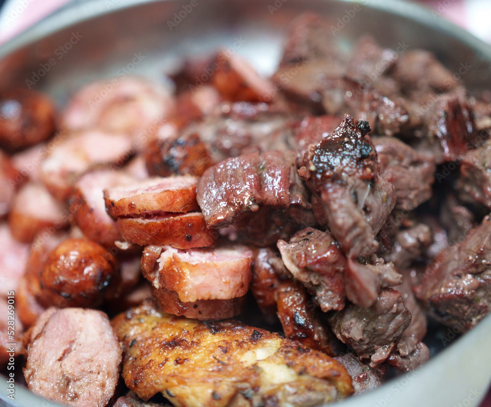 pedaços de carne bovina e linguiça de porco assados e servidos dentro de uma bandeja sobre a mesa