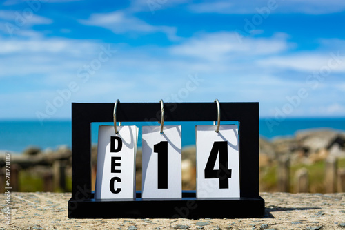 Dec 14 calendar date text on wooden frame with blurred background of ocean.