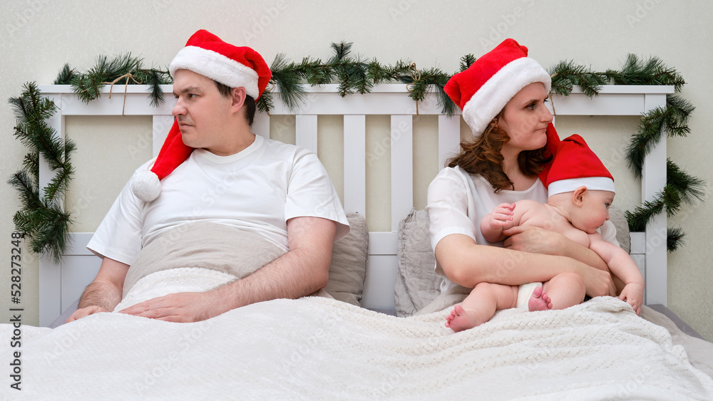 Obraz premium Quarrel of husband and wife with baby on bed decorated for christmas and new year, family couple in home bedroom