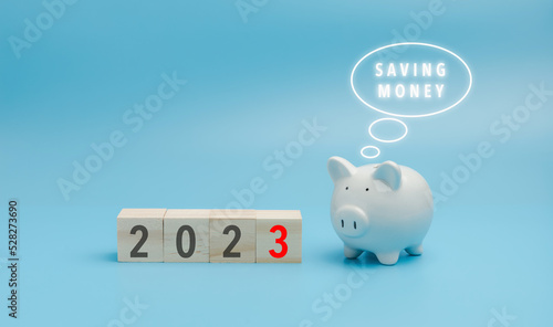 2023 on a wooden block cube with the white piggybank on blue background with copy space. The white piggy bank thinking of 2023 set target saving of money.