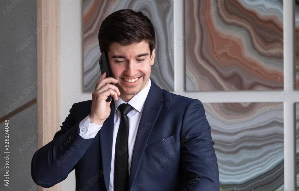 young businessman in a dark blue suit working in the office, talking by mobile phone young businessman in a dark blue suit working in the office, talking by mobile phone