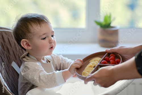 Fotografie, Obraz Mother gives toddler baby fruits and berries on a plate