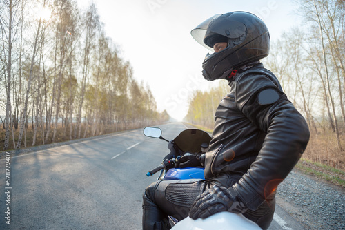 Motorbiker in the helmet stands on the empty road.