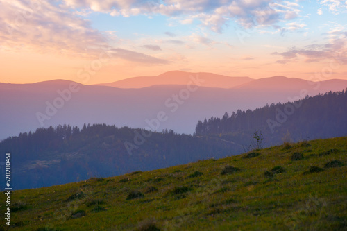 mountainous countryside at dusk. green grassy rolling hills on an autumn evening. carpathian rural scenery. view in to the distant ridge beneath a glowing sky with clouds