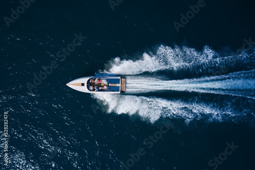 A white large open boat with people is moving quickly on dark water. Top view. White speedboat fast movement on dark water top view.