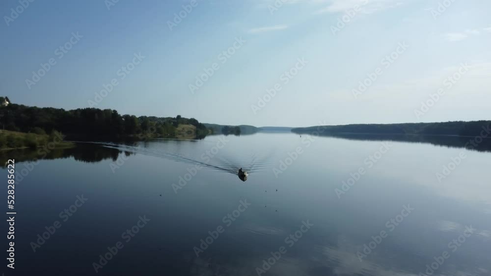 Silhouette of a motor boat with a fisherman moving along the smooth surface of the river. Complete calm on a wide navigable river. Silhouette of a motor boat with a fisherman moving along the smooth surface of the river. Complete calm on a wide navigable river.