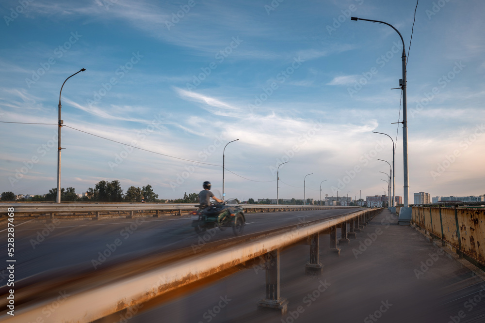 A man on a motorcycle with a sidecar rides over the bridge into the city. Active lifestyle.