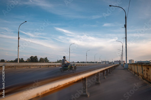 A man on a motorcycle with a sidecar rides over the bridge into the city. Active lifestyle. © Uladzimir