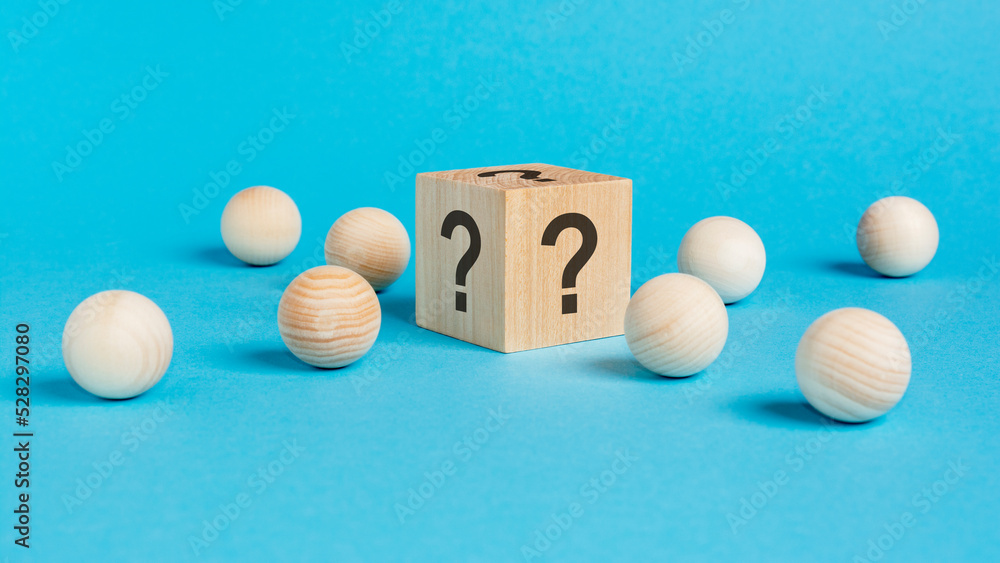 wooden cube with a question mark surrounded by wooden balls on a blue table background