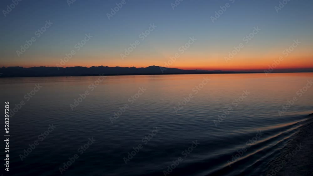 Gentle ship wake rolls in ripples on smooth water at beautiful orange sunset against deep blue sky as dusk settles over the inside passage to Alaska Gentle ship wake rolls in ripples on smooth water at beautiful orange sunset against deep blue sky as dusk settles over the inside passage to Alaska