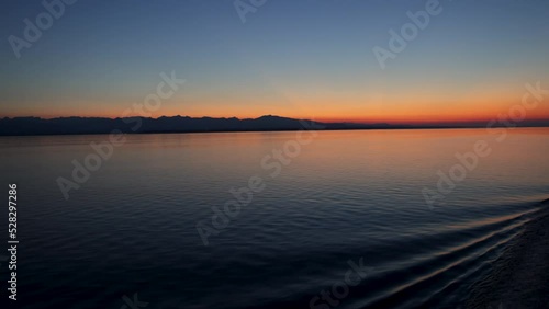 Gentle ship wake rolls in ripples on smooth water at beautiful orange sunset against deep blue sky as dusk settles over the inside passage to Alaska