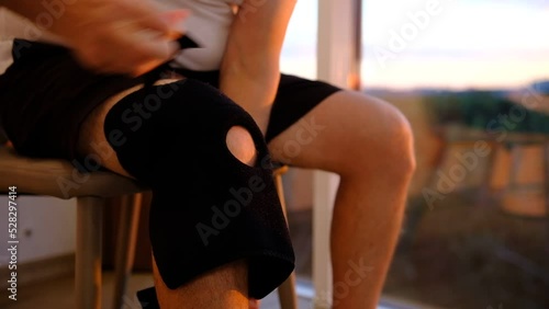close up of knee support brace on leg of a man in sunset lights near the window. Massage leg in place of pain,
