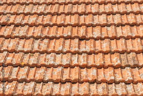 Old orange tiles on the roof of the house. The old ceramic coating of the roof of the house from water and moisture. Tile close-up.