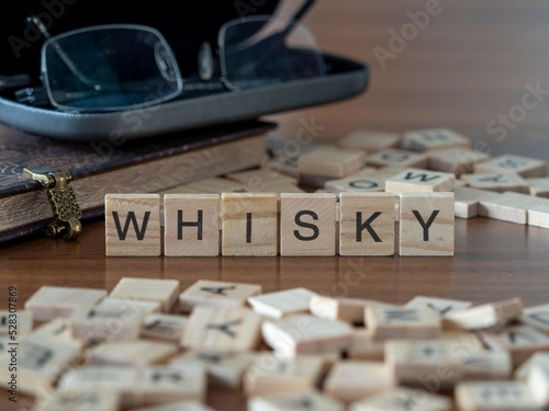 whisky word or concept represented by wooden letter tiles on a wooden table with glasses and a book