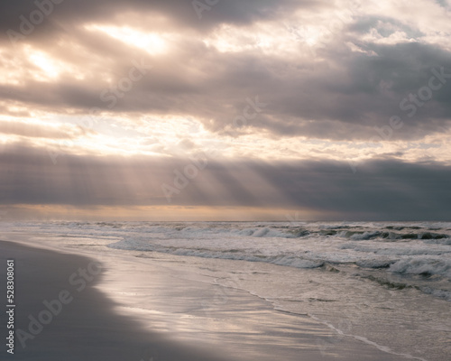 An early morning walk on the beach with misty sun rays and a cloudy and glowing sky at the ocean. 