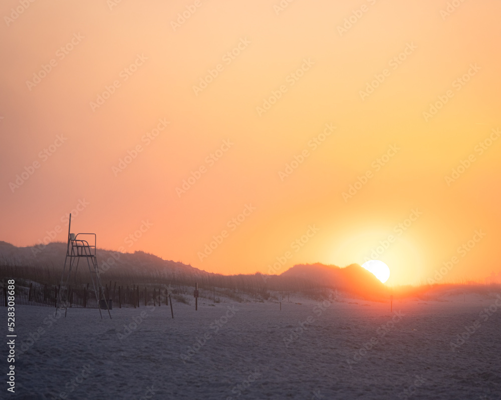 early morning sunrise along the coast of Florida. The sun is peaking over the sand dunes. There is an empty lifeguard station.