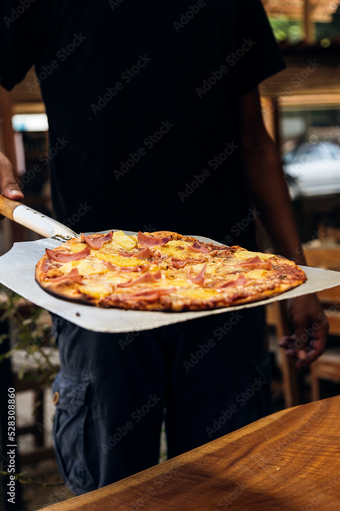 Restaurant worker shows pizza fresh from the oven on a tray