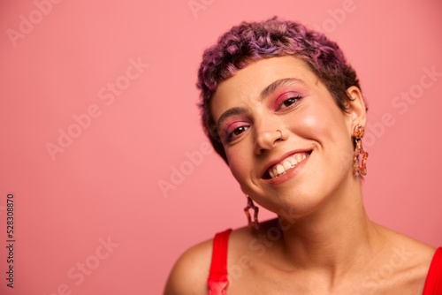 Fashion portrait of a woman with a short haircut of purple color and a smile with teeth in a red top on a pink background dancing happily