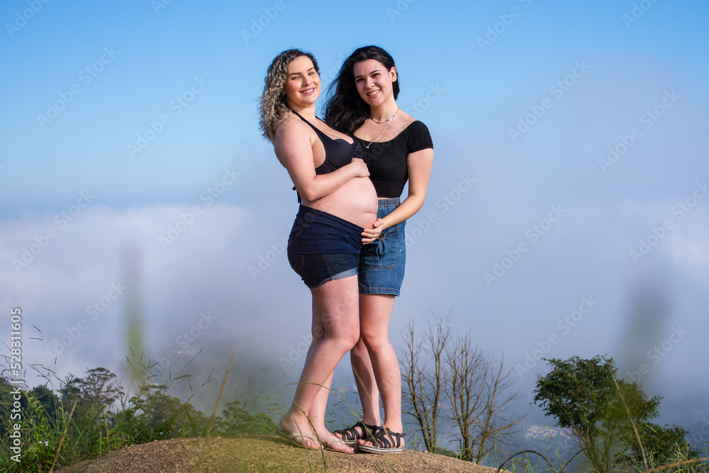 pregnant lesbian couple showing belly outdoors.