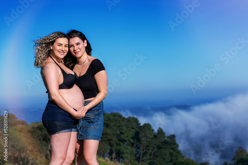 romantic pregnant lesbian couple showing and caressing belly outdoors.