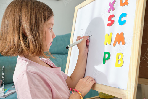 little girl drawing and learning the letters on a blackboard at home. Learn having fun.