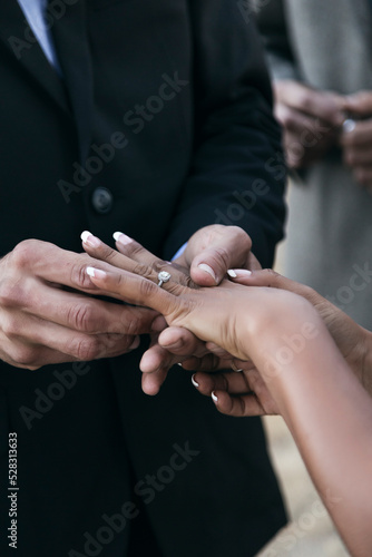 Bride and groom putting rings on each other's fingers during outdoor wedding.