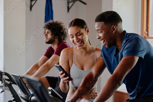 Three young multiracial friends laughing while on mobile phone at the gym