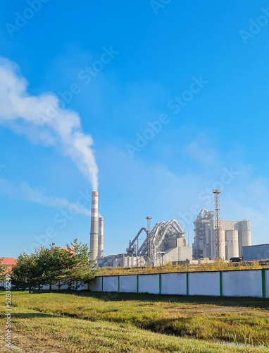 The factory spews smoke from its pipes against a backdrop of clear blue skies, pollution