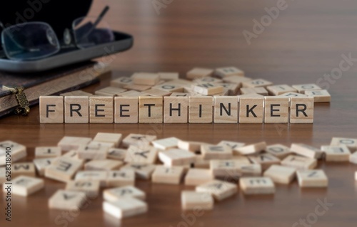 freethinker word or concept represented by wooden letter tiles on a wooden table with glasses and a book
