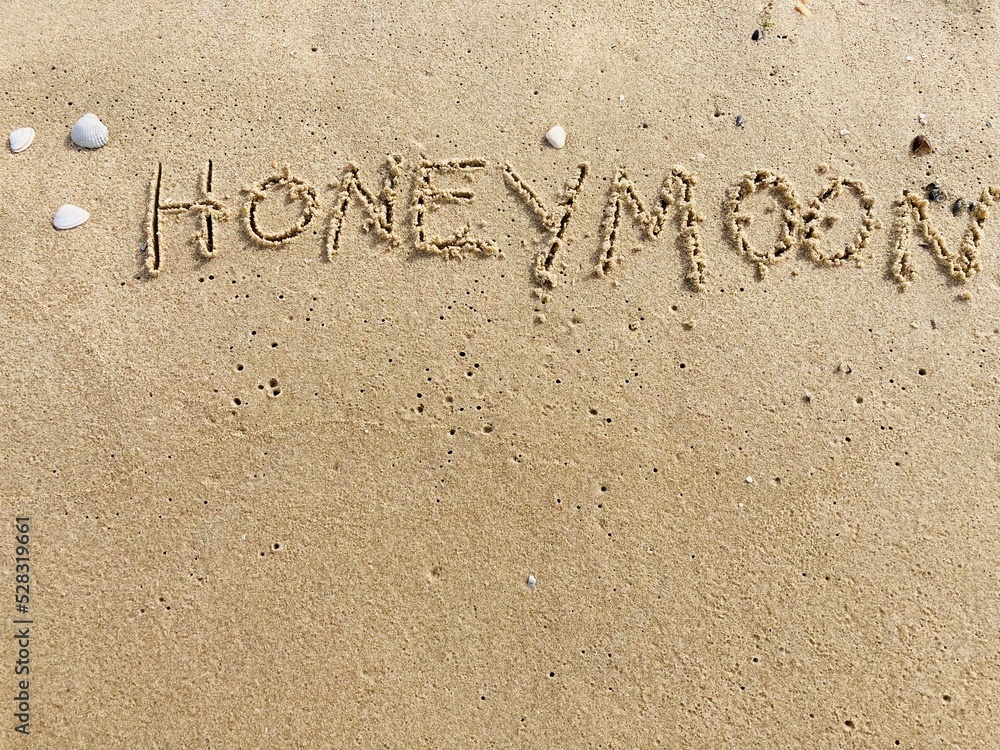 Fototapeta premium on the beach is carved with letters in the smooth sand the writing Honeymoon