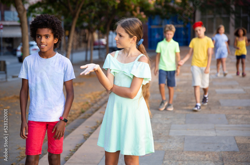 Young african-american boy and caucasian girl walking during summer day and having conversation.