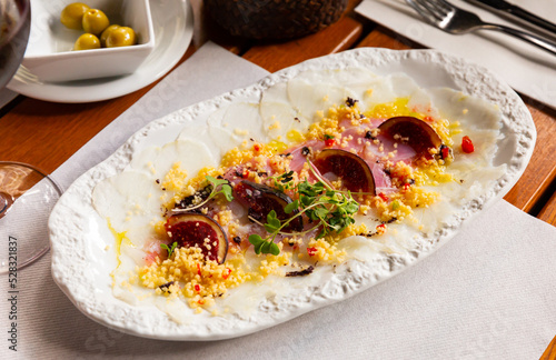 Delicious cod carpaccio with fresh figs and citrus sauce served on white plate. Fish appetizer