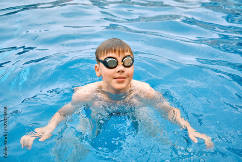Smiling boy portrait in swimming goggles, Child swim in the pool, sunbathes, swimming in hot summer day. Relax, Travel, Holidays, Freedom concept. 