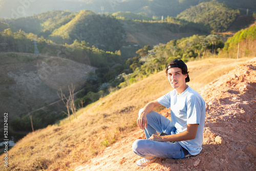 Portrait of a young man sitting on top of a mountain and enjoying nature.