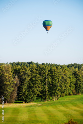 Colorful balloons fly over the green landscape of the field and trees