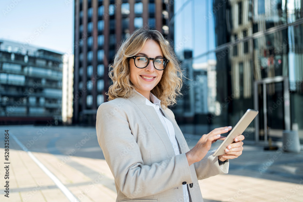 Fototapeta premium The manager is a happy woman who answers the client's email using a tablet. Glasses on his face, goes to work in a new office.