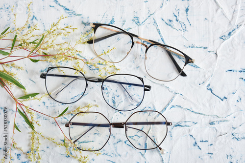 Woman's eyeglasses and little yellow flowers branches on textured background. Flat lay