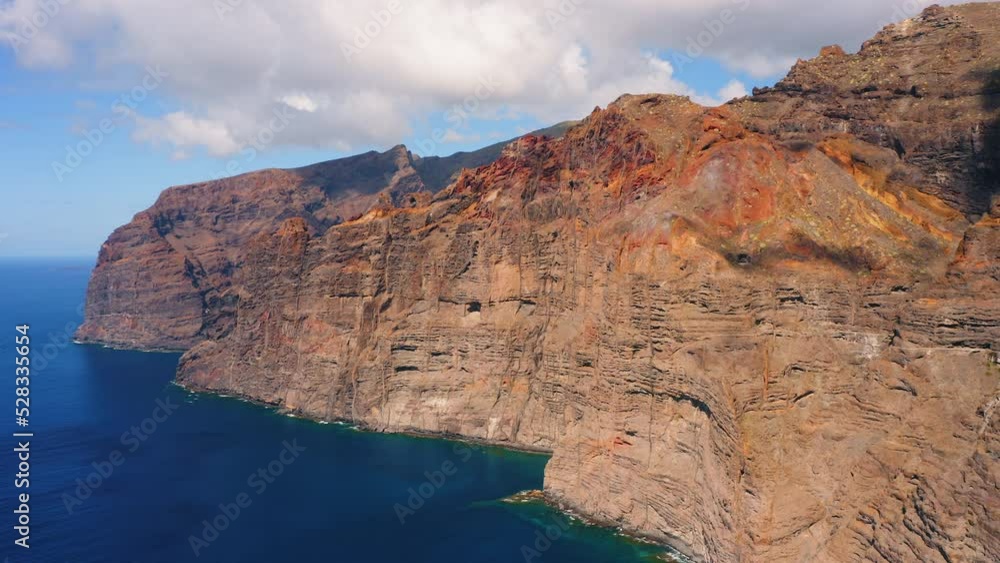 Drone flight over peaks of high rock Los Gigantes in Tenerife island. Spain. Barren mountains range on seaside. Travel to the paradise spectacular volcanic rocky cliff beach. Sunny day. Go everywhere. Drone flight over peaks of high rock Los Gigantes in Tenerife island. Spain. Barren mountains range on seaside. Travel to the paradise spectacular volcanic rocky cliff beach. Sunny day. Go everywhere.