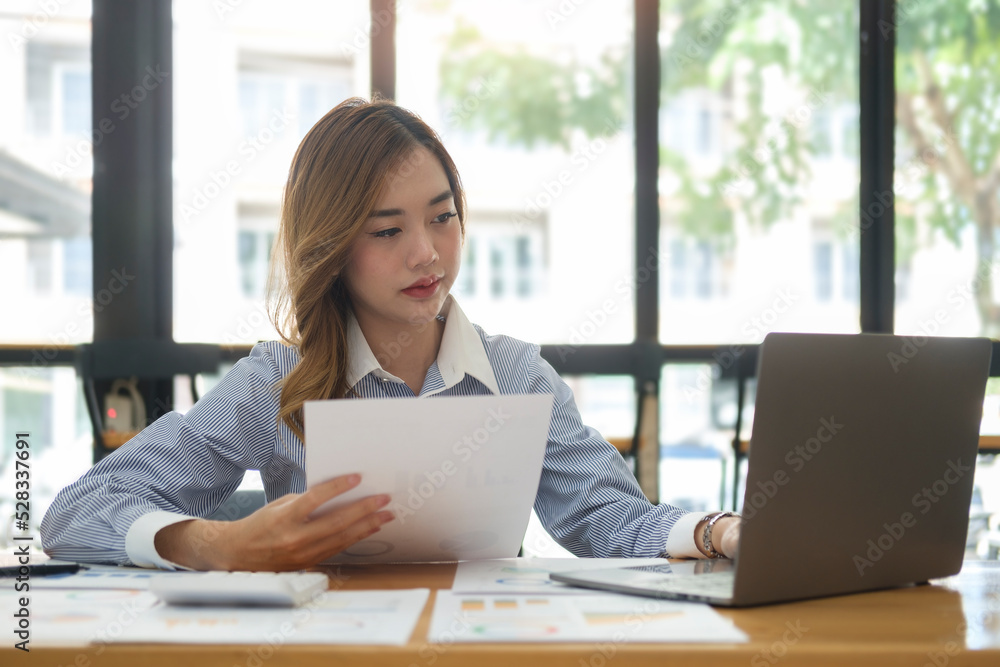 Beautiful asian businesswoman using laptop computer and checking financial document at office desk.. Beautiful asian businesswoman using laptop computer and checking financial document at office desk..