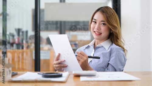 Attractive young woman office worker holding document, working at her office desk.