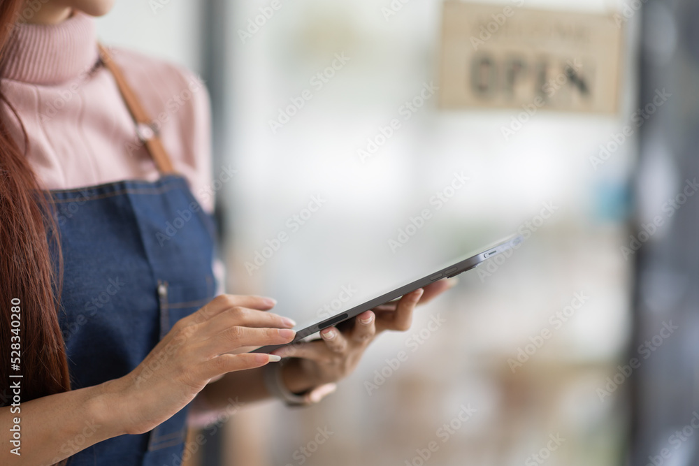 Portrait of a friendly young asian business woman barista wearing apron and standing with her arms crossed at the door of a trendy cafe, open sign barista SME entrepreneur seller concept