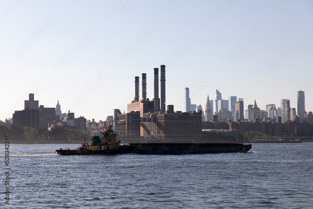 Tugboat barge on East River with view of power plant in Manhattan.