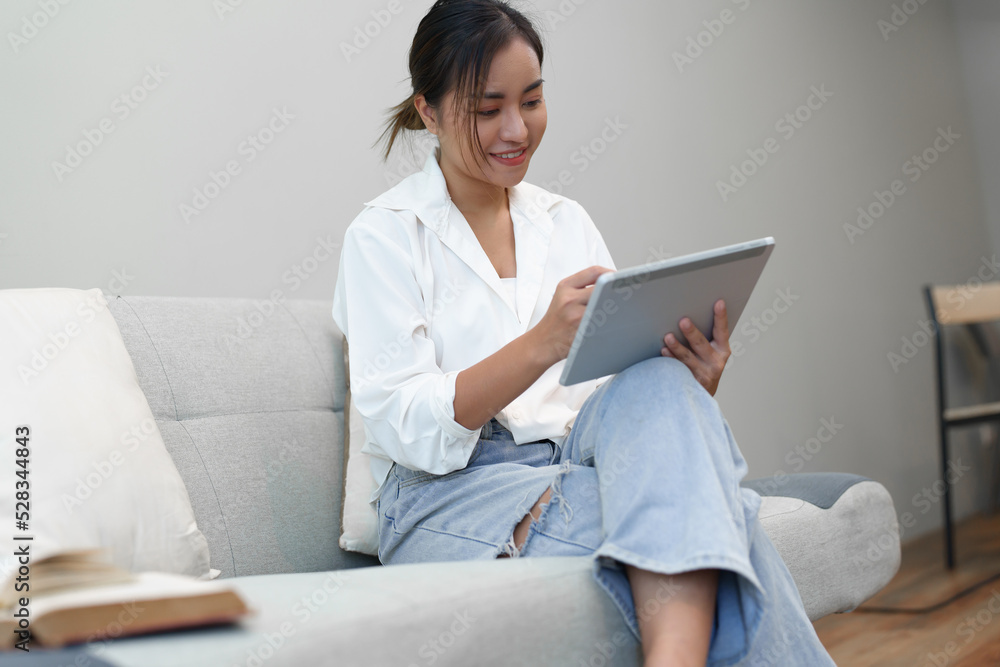 Portrait of a young Asian woman sitting on the sofa using a tablet. Portrait of a young Asian woman sitting on the sofa using a tablet.